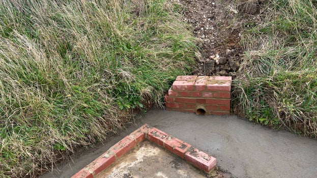 An image of a drain to a soakaway, with low brick walls to deflect floodwater into the drain